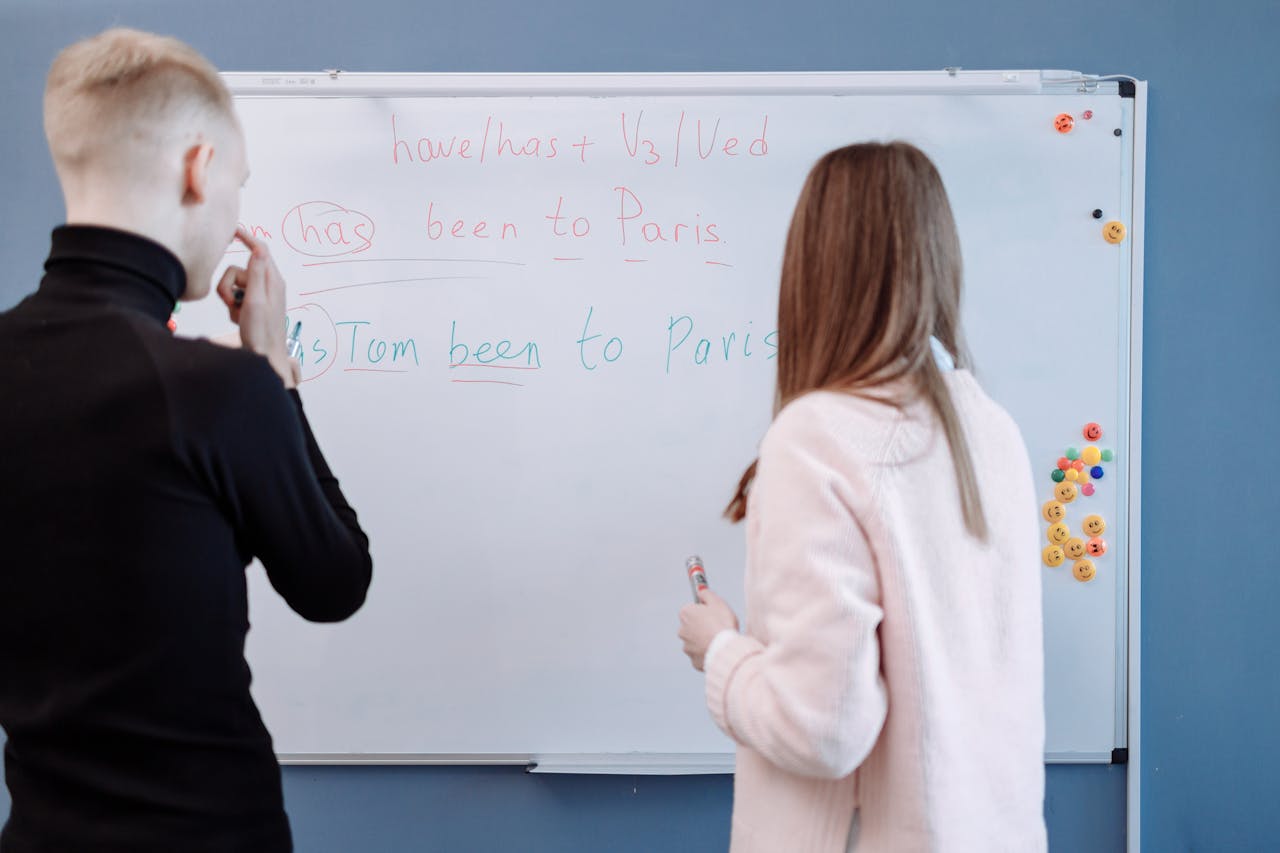 about-02 Two students studying English grammar at a whiteboard in a classroom setting.
