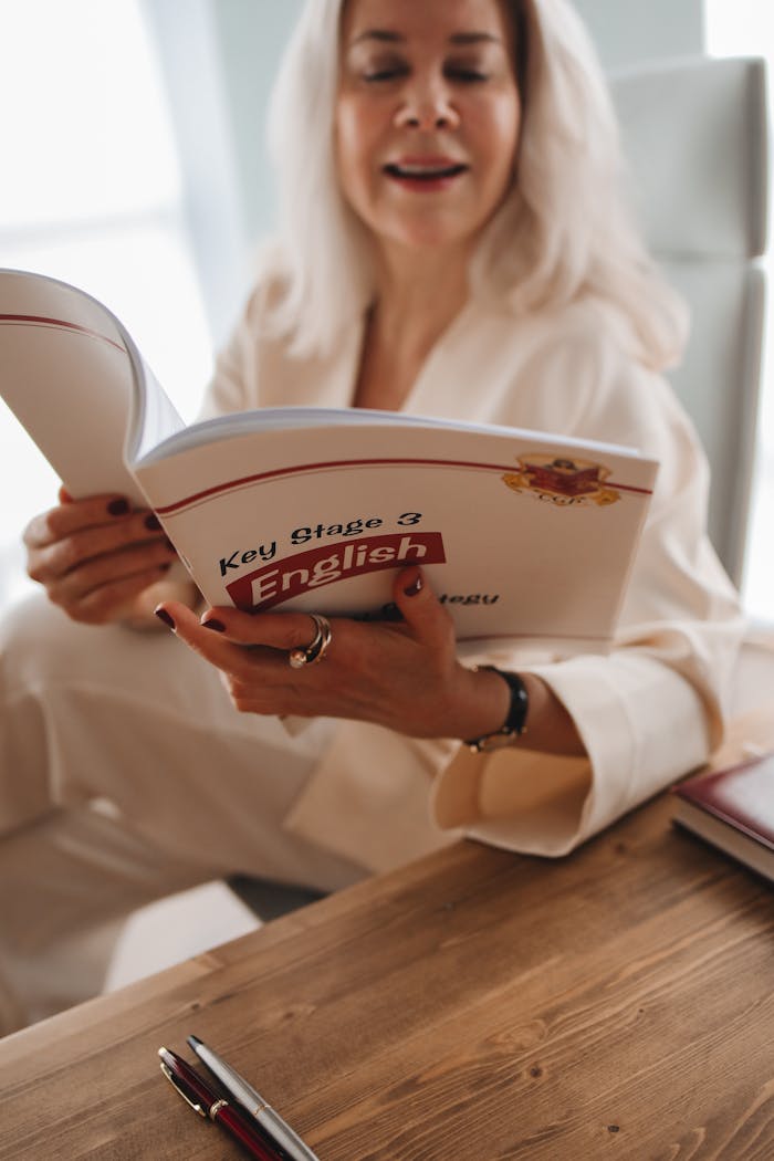 services-img Adult woman reading a Key Stage 3 English book, seated at a wooden table.