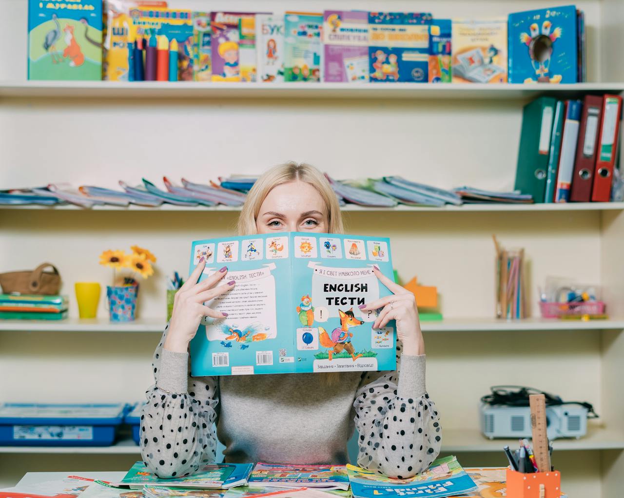 services-01 Woman reading an English book in a colorful classroom setting.